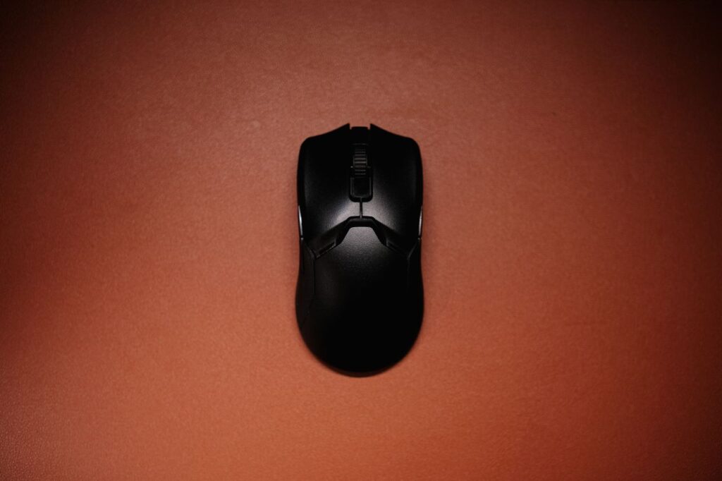 A top view of a sleek black wireless mouse on a red background, highlighting modern technology.