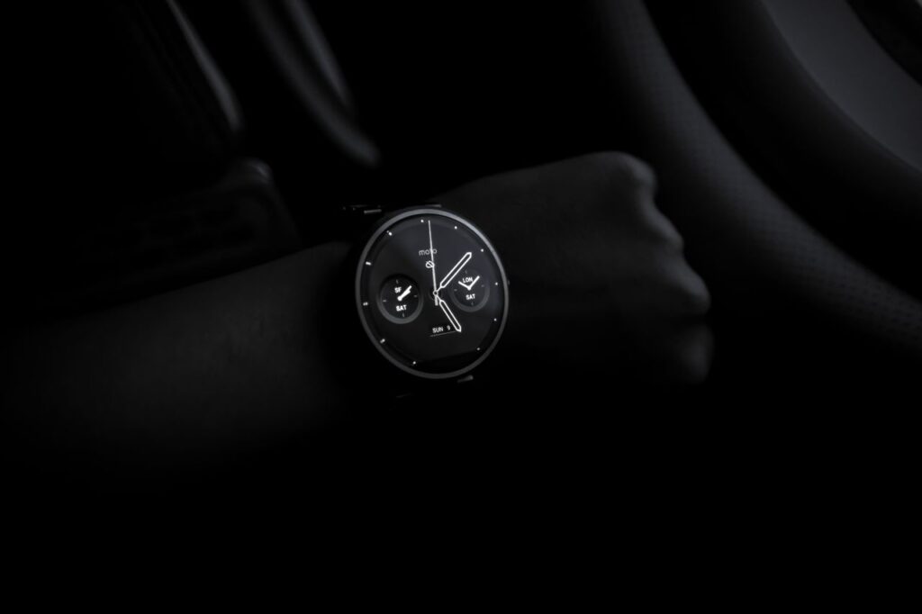 A sleek Moto 360 smartwatch showing time on a wrist in a dimly lit setting, emphasizing its modern design and technology.